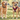 Two dogs in a park: a golden retriever wearing a patterned collar with an ID tag, and a tan dog wearing a red and navy harness with an ID tag.